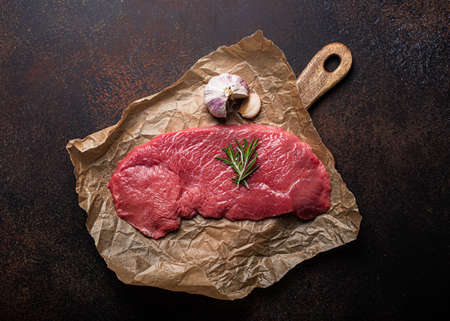 Beef lean raw fillet steak on baking paper with rosemary, garlic and spices