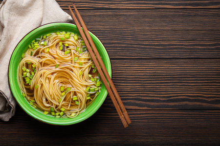 Asian noodles soup in green rustic ceramic bowl with wooden chopsticks top view on dark wooden background. Lo mein noodles with broth, green onionの写真素材