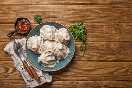 Georgian dumplings Khinkali on plate with red tomato sauce and fresh cilantro top view, rustic wooden background, traditional dish of Georgia, space for textの写真素材
