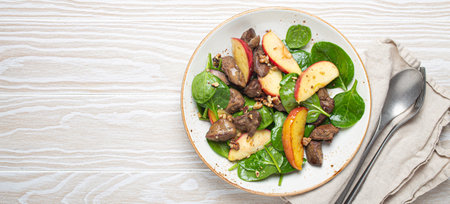 Healthy Salad with Iron Rich Ingredients Chicken Liver, Apples, Fresh Spinach and Walnuts on White Ceramic Plate, White Wooden Background Top View.の写真素材
