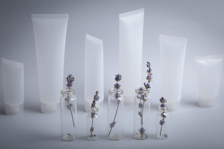 Lavender sprigs in glass test tubes and empty plastic cosmetic tubes staying at gray background, beauty concept of cosmetology, body and skincare. Botanical natural cosmetic ingredientの写真素材