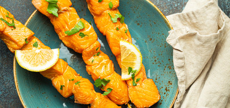Grilled barbecue salmon skewers seasoned with green parsley and lemon on ceramic plate on dark blue concrete rustic table background top view, healthy eatingの写真素材