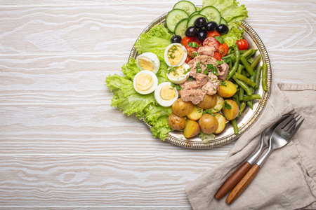 Nicoise salad with tuna, eggs, potatoes, green beans, and olives on a white table with copy spaceの写真素材
