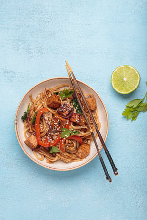 Bowl of vegetarian udon noodles with fried tofu and vegetables is served with chopsticks