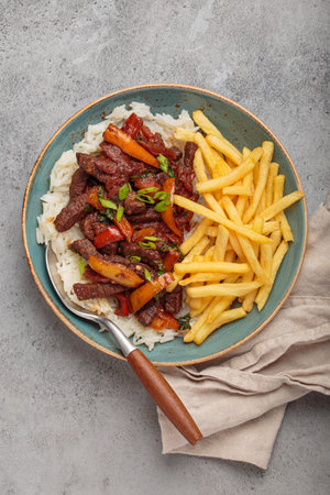 Lomo saltado, traditional Peruvian dish, with french fries served on a plate with rice