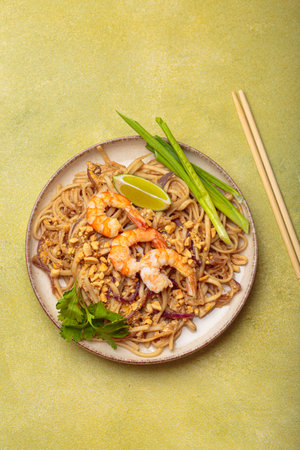 Bowl of pad thai noodles garnished with shrimps and lime on green background, traditional dish of Thailandの写真素材