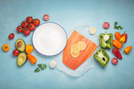 Fresh salmon with vegetables and empty plate lying on blue backgroundの写真素材