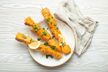 Grilled barbecue salmon skewers seasoned with green parsley and lemon on ceramic plate on white wooden rustic table background top view, healthy eatingの写真素材