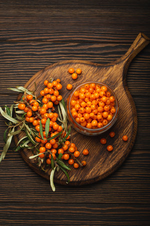 Sea buckthorn ripe berries in glass jar and branches with leaves top view on dark wooden rustic...
