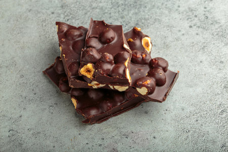 Pieces of dark chocolate with hazelnuts resting on gray surface