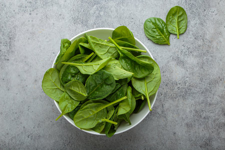 Fresh spinach leaves resting in white bowl on gray background top view,
