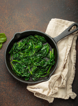 Healthy steamed spinach in cast iron pan on brown rustic background top viewの写真素材