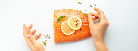 Female hands seasoning fresh raw salmon marbled fillet isolated on white background with lemon, coarse salt, green herbs top view. Healthy nutrition and balanced dietの写真素材