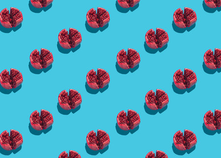 Modern pattern of pomegranate halves showing red seeds on vibrant blue background, high contrast with hard lightの写真素材