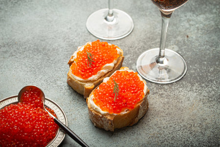 Small metal plate with red salmon caviar, two caviar toasts canape, two glasses of champagne top view on grey concrete background, festive luxury delicacy and appetizerの写真素材
