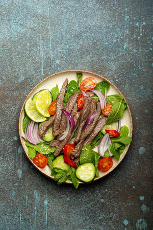 Plate with traditional Thai beef salad with vegetables and mint top view served on rustic concrete stone background, healthy exotic asian mealの写真素材