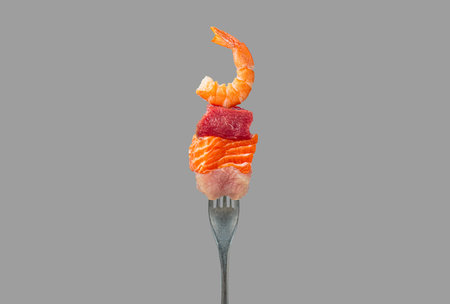 Fork holding pieces of raw salmon, beef, chicken and shrimp representing protein sources isolated on grey backgroundの写真素材