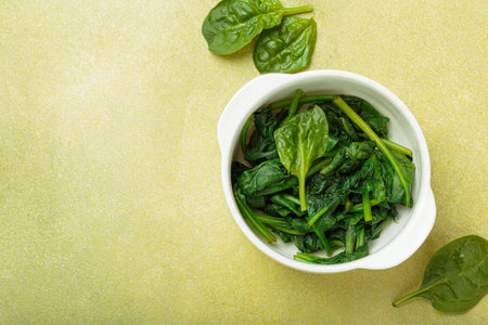 Steamed spinach leaves in white bowl on table top view on green background, healthy food or diet, space for textの写真素材
