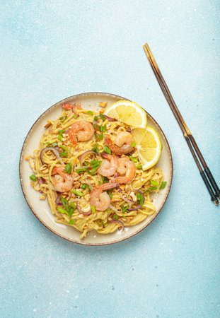 Pad thai noodles with shrimps and chopsticks on light blue background, traditional dish of Thailand