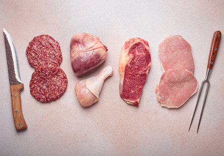 Selection of assorted raw meat cuts for zero carb carnivore diet: uncooked beef steak, pork meat, ground meat patty, heart, and chicken legs on beige stone background top viewの写真素材