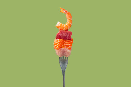 Diverse protein sources on a fork, pieces of raw salmon, beef, chicken and shrimp on green...