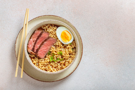 Ramen or asian style noodles soup with beef, egg and green onions in bowl on light beige background top view, space for textの写真素材