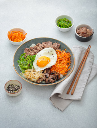 Traditional korean bibimbap with fried egg, beef and vegetables and other toppings on light background with chopsticksの写真素材