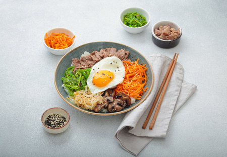 Traditional korean bibimbap with fried egg, beef and vegetables and other toppings on light background with chopsticksの写真素材