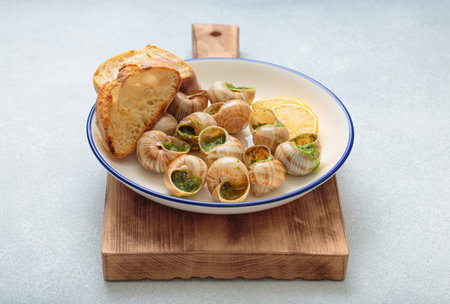 Escargots snails with garlic butter, parsley and lemon wedges on white plate on light backgroundの写真素材