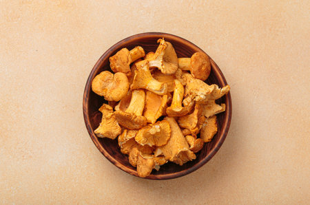Fresh chanterelle mushrooms in a rustic bowl on warm beige background top viewの写真素材