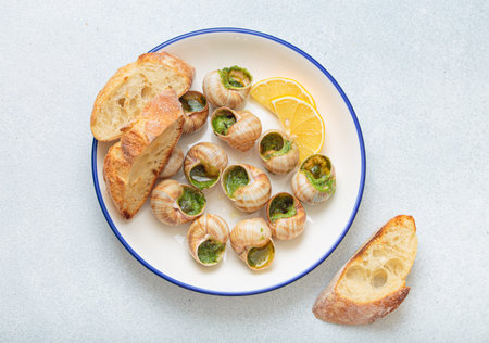 Escargots de bourgogne snails with garlic butter, parsley and lemon wedges on white plate on light backgroundの写真素材