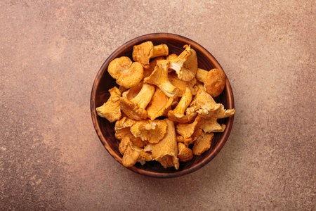 Fresh chanterelle mushrooms in a rustic bowl on brown background top viewの写真素材