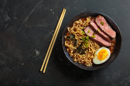 Ramen soup with beef, egg, and chopsticks on dark background top view, space for textの写真素材