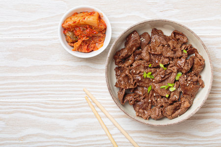 Bulgogi, grilled marinated beef Korean dish with kimchi and sesame seeds top view on white wooden background, space for textの写真素材