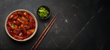 Traditional Korean tteokbokki served on white plate with chopsticks and sesame seeds on black rustic background, space for textの写真素材