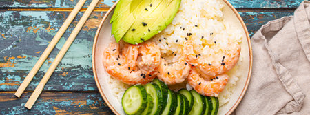 White ceramic bowl with rice, shrimps, avocado, vegetables and sesame seeds and chopsticks on colourful rustic wooden background top view. Healthy asian style poke bowlの写真素材