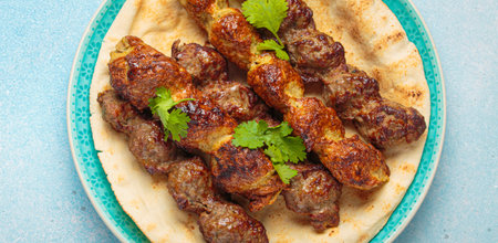 Kofta meat kebabs with pita bread, tomato sauce, and coriander on blue plate top view on light beige...