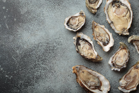 Fresh opened oysters scattered on dark gray surface top view with space for text