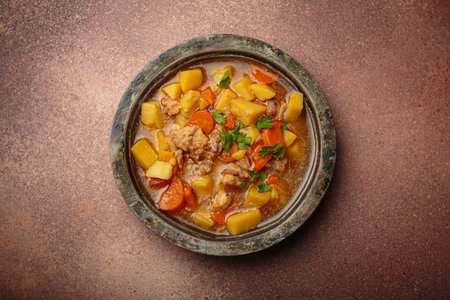 Chicken stew or soup with potatoes and carrots served in rustic bowl with spoon top view on dark brown concrete backgroundの写真素材