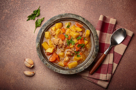 Chicken stew or soup with potatoes and carrots served in rustic bowl with spoon top view on dark brown concrete backgroundの写真素材