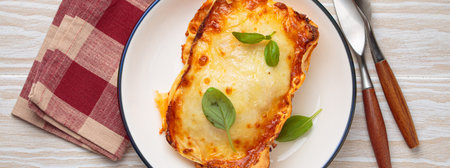 Italian lasagna with cheese and basil on plate on white rustic wooden background top viewの写真素材