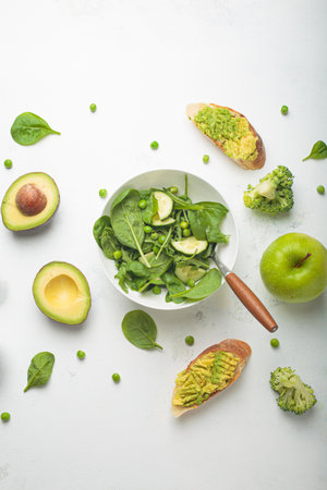 Fresh salad bowl, avocado toasts, raw green vegetables fruit white background top view, diet, vegetarian healthy foodの写真素材