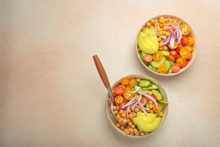 Two bowls with vibrant vegetarian chickpea salad with fresh vegetables in ceramic bowls top view on light beige background, space for textの写真素材
