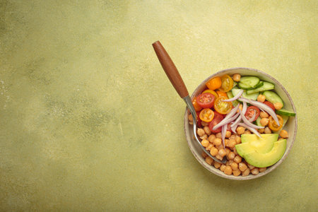 Vibrant vegetarian chickpea salad with fresh vegetables in ceramic bowl top view on light green...