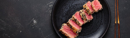 Seared grilled tuna steak tataki slices sesame seeds lemon black plate healthy delicacy space for textの写真素材
