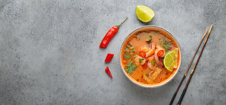 Spicy tom yum soup with shrimps, lime, chili pepper and coriander served in bowl top view,...