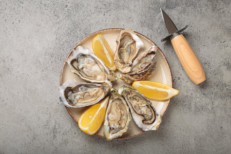Fresh oysters with lemon wedges and oyster knife on plate top view