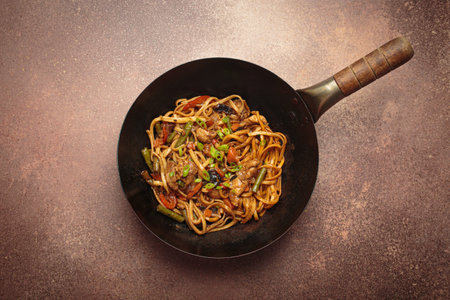 Asian style stir fry noodles with chicken and vegetables in a black wok pan with chopsticksの写真素材