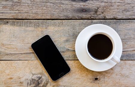 top view cup of coffee and smartphone on wood table backgroundの写真素材