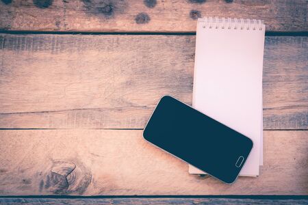 paper note and mobile phone on wood background in vintage style